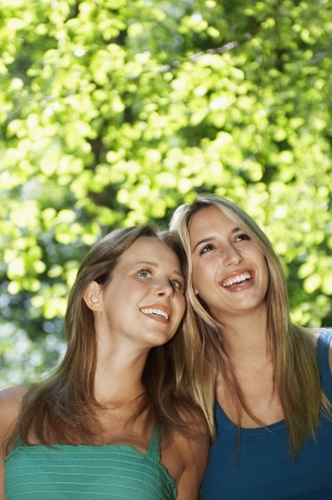 Two young women standing in forest looking up, front viewの写真素材