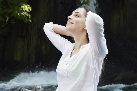 Young woman pulling back hair by river in forest, side viewの写真素材