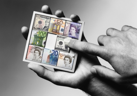 Man holding sliding tile puzzle with tiles representing various currencies, close-up of hands,...