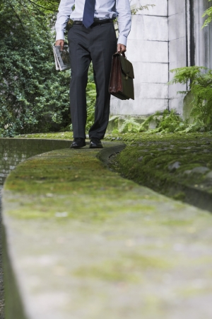 Businessman walking on wall in park low sectionの写真素材