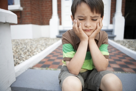 Sad little boy sitting on front steps of house close upの写真素材