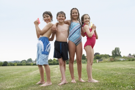 Two young girls and boys in swimsuits in field holding water pistols portraitの写真素材