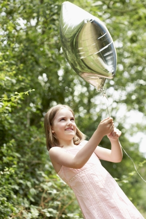 Girl in park playing in park with helium filled balloonの写真素材