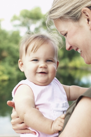 Mother holding daughter by lake head and shouldersの写真素材