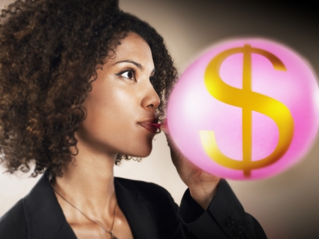 Businesswoman blowing up balloon with dollar sign on head and shouldersの写真素材