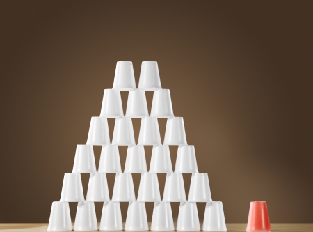 Pyramid of white plastic cups on table next to single red cupの写真素材