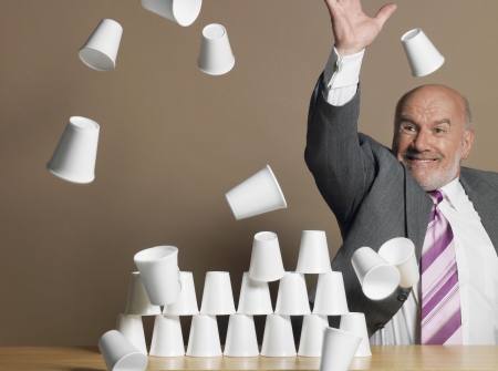 Businessman knocking down pyramid of plastic cupsの写真素材