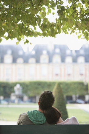 Young woman leaning on young man sitting on bench in park back viewの写真素材