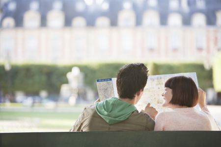 Young couple sitting on bench looking at map in park back viewの写真素材