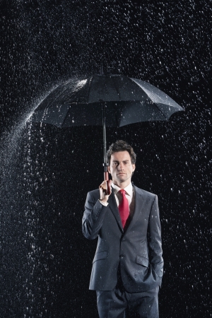 Businessman standing under sturdy Umbrella hand in pocketの写真素材