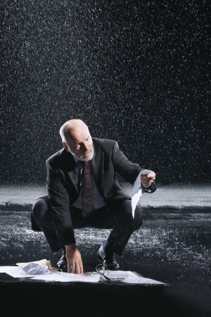 Businessman Picking up soaked Paperwork during downpourの写真素材