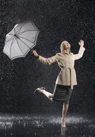 Woman standing on one leg holding umbrella leaning into falling rainの写真素材