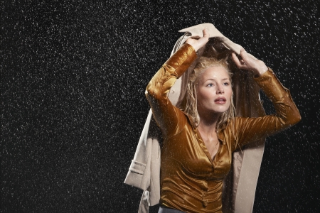 Businesswoman covering head with jacket during rainstormの写真素材