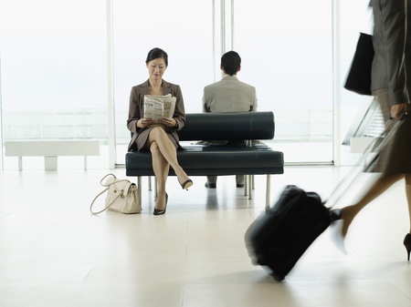 Businesswoman sitting on bench in airport reading newspaperの写真素材