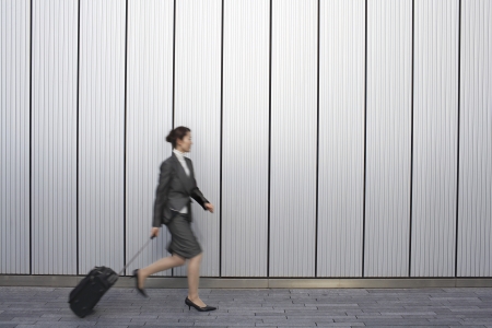 Businesswoman walking outdoors pulling suitcase behind her side viewの写真素材
