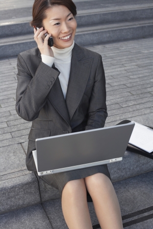Businesswoman on outdoor Steps Using Laptop and talking on mobileの写真素材