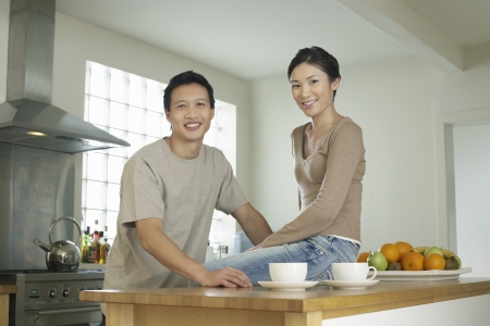 Young Couple husband standing wife sitting on bar in Kitchen portraitの写真素材