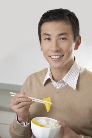 Young Man Eating Rice and Peppers with chopsticksの写真素材