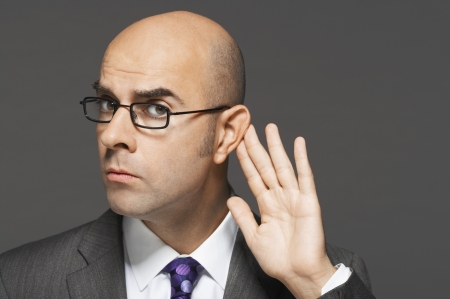 Balding man with hand behind ear listening closelyの写真素材