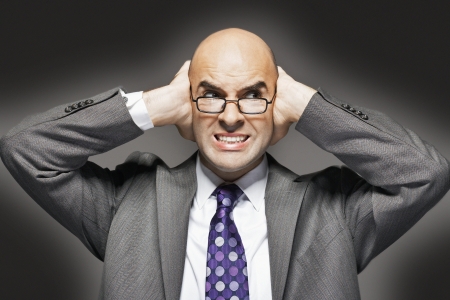 Bald businessman holding hand over ears looking sideways making a faceの写真素材