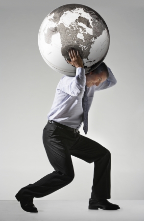 Businessman struggling carrying globe on shoulders side viewの写真素材