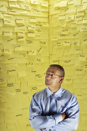 Middle-aged man in glasses standing in front of wall covered in sticky notesの写真素材