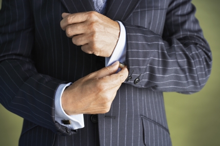 Middle-aged businessman in full suit buttoning buttons on shirt  mid sectionの写真素材