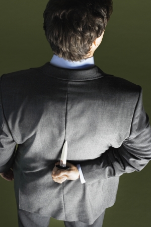 Mid-adult businessman standing holding knife behind back back viewの写真素材