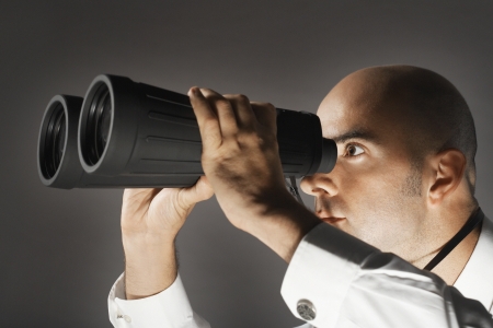 Balding Middle-aged businessman looking through large binocularsの写真素材