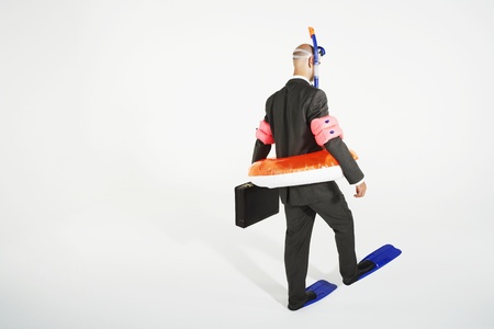 Middle-aged businessman in flippers inflatable rubber ring snorkel and goggles walking carrying briefcaseの写真素材