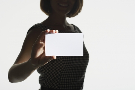 Smiling silhouetted woman standing holding large blank card mid sectionの写真素材