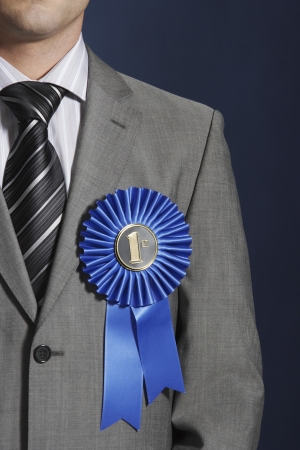 Man wearing blue ribbon on lapel against dark background mid sectionの写真素材