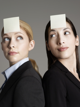 Portrait of two female office workers with sticky notes on foreheadの写真素材
