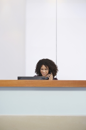 Receptionist sitting behind reception desk talking on Telephoneの写真素材