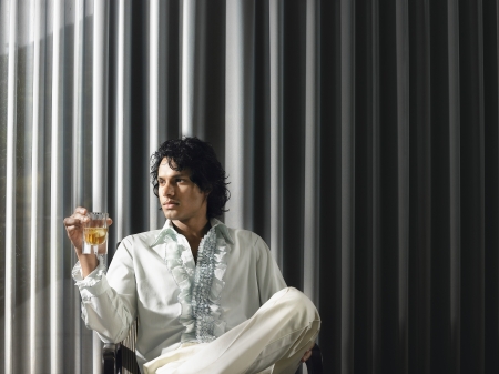 Man sitting with alcoholic drink in front of curtains