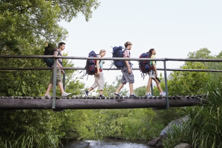 Four teenagers (16-17 years) backpacking in forest crossing wooden bridge side viewの写真素材