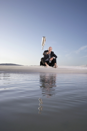Business man sitting on beach throwing message in bottle into sea low angle viewの写真素材