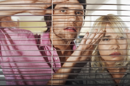 Young woman and man looking through Venetian Blinds front view.の写真素材