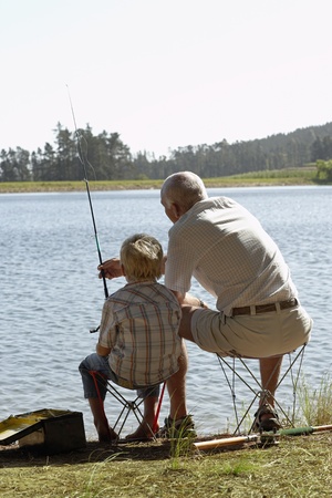 Boy (7-9) fishing with grandfather back view.の写真素材