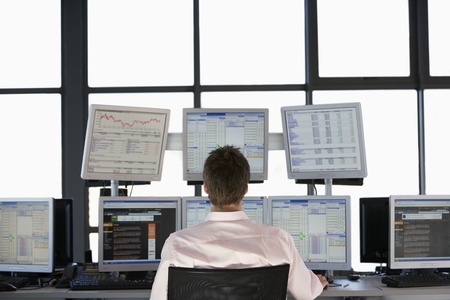 Businessmen sitting at desk watching computer screens back view.の写真素材