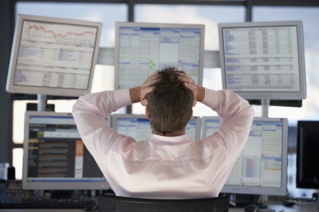 Businessman watching computer screens with hands on head back view.の写真素材