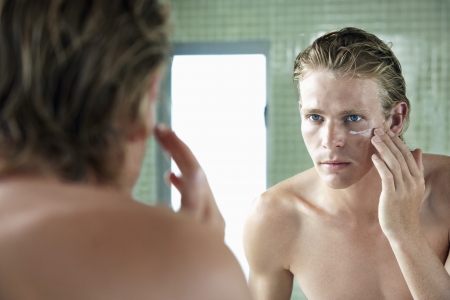 Man applying facial cream in front of mirrorの写真素材