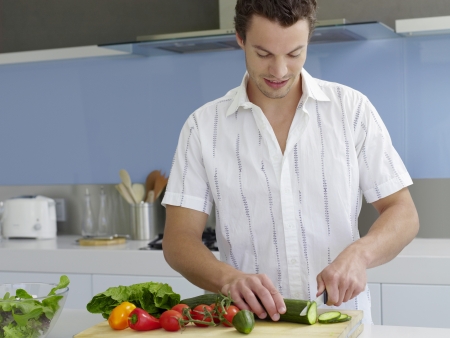 Young man cutting vegetables on cutting board in kitchenの写真素材