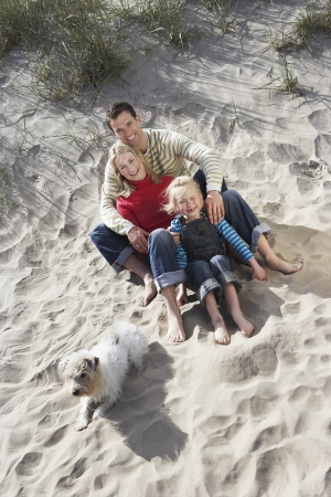 Parents embracing daughter (5-6) with dog on beach portraitの写真素材