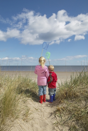 Brother and sister (4-6) with fishing nets standing on sand dunesの写真素材