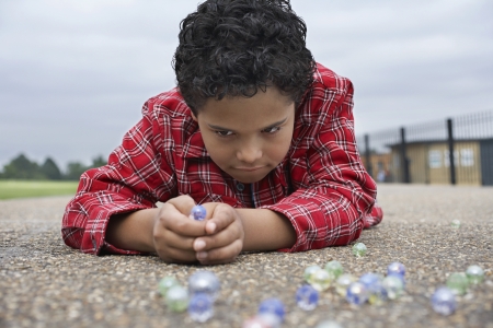 Boy (7-9) playing marbles lying in playgroundの写真素材
