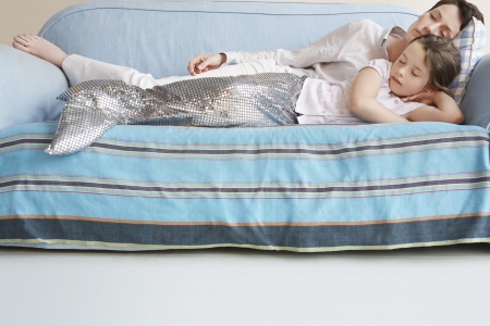 Young girl (5-6) wearing mermaid costume sleeping on sofa with motherの写真素材