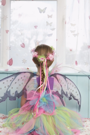 Young girl (5-6) wearing fairy costume looking through window back viewの写真素材
