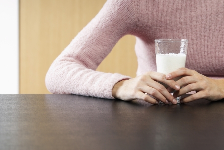 Woman holding glass of milk on table mid sectionの写真素材
