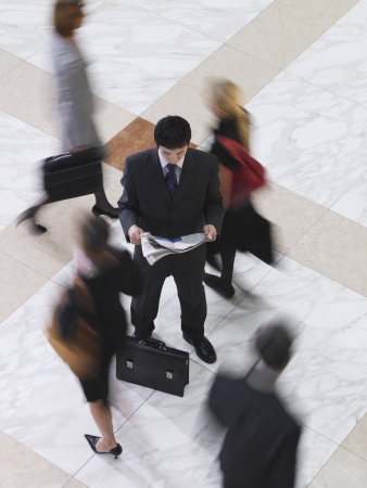 Business man reading newspaper amongst people walking elevated view long exposureの写真素材